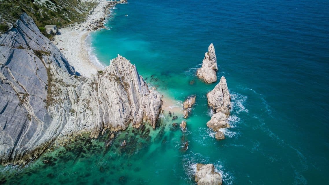 Una vista aerea di imponenti scogliere bianche e faraglioni che sporgono da acque turchesi lungo una costa frastagliata.