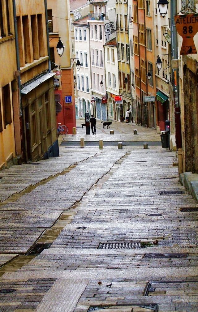 Una vista lungo una ripida e bagnata strada acciottolata con gradini integrati, fiancheggiata da alti, colorati e storici edifici europei.
