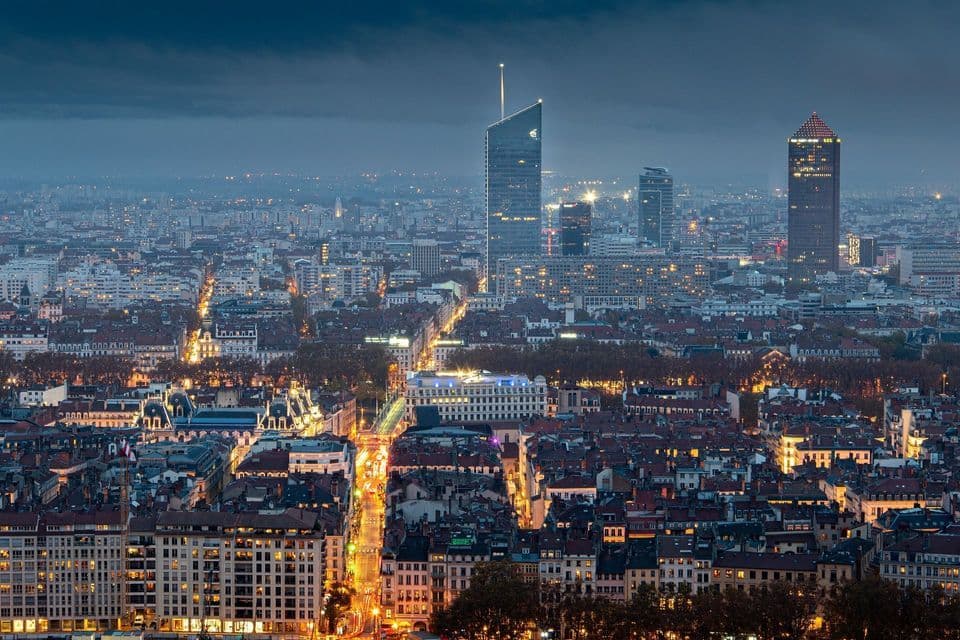Una veduta dall'alto di un'ampia città al crepuscolo, con strade illuminate e grattacieli sotto un cielo nuvoloso.