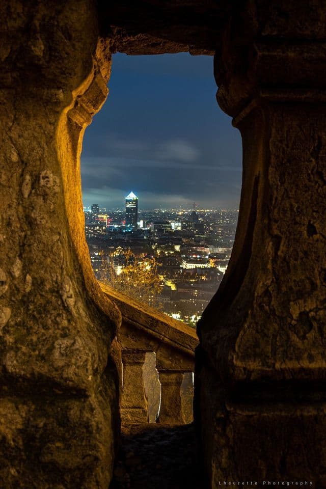 Uno skyline cittadino illuminato a giorno di notte, ammirato attraverso un varco tra due grandi pilastri di pietra erosi.