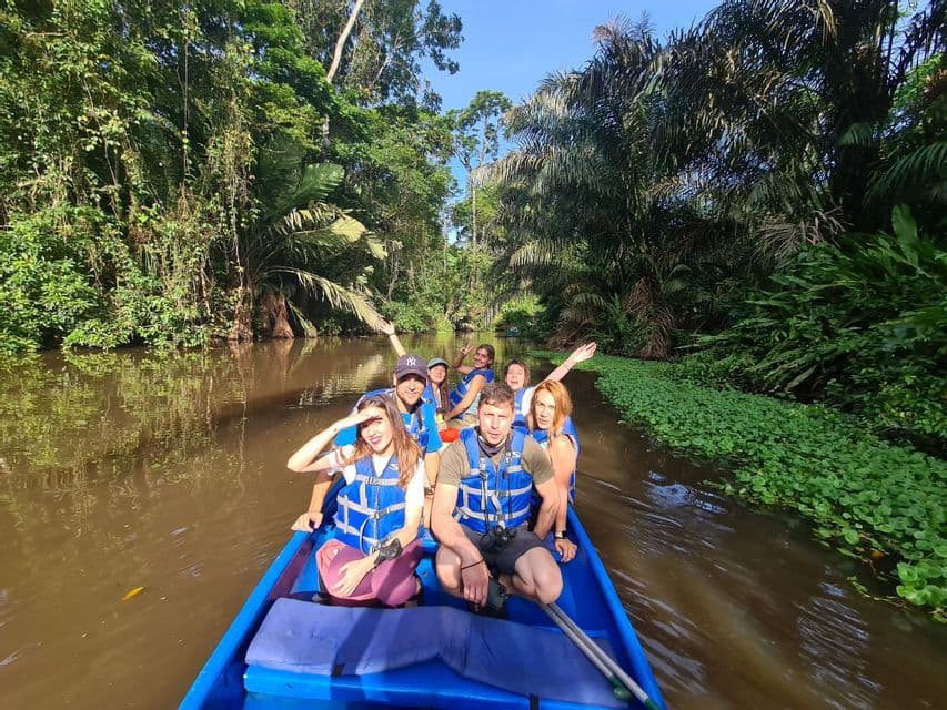 Un voyage de groupe WeRoad navigue sur une rivière de jungle dans un bateau bleu, au milieu d'un feuillage tropical dense.