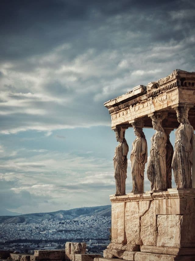 Four ancient caryatid statues serve as columns on a temple porch, overlooking a city under a dramatic, cloudy sky.