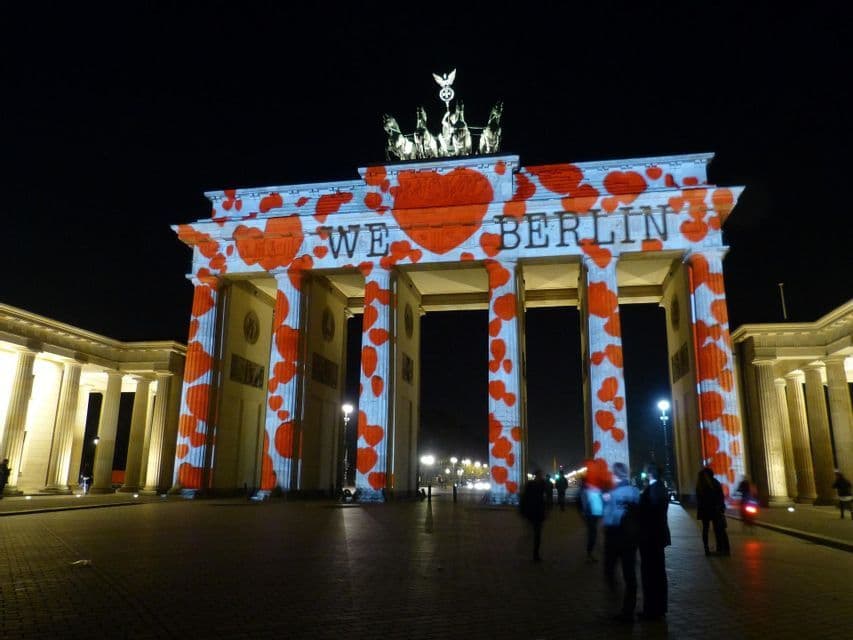 La Porta di Brandeburgo di notte, illuminata con una proiezione di cuori rossi e le parole 'WE BERLIN' sulla sua facciata.