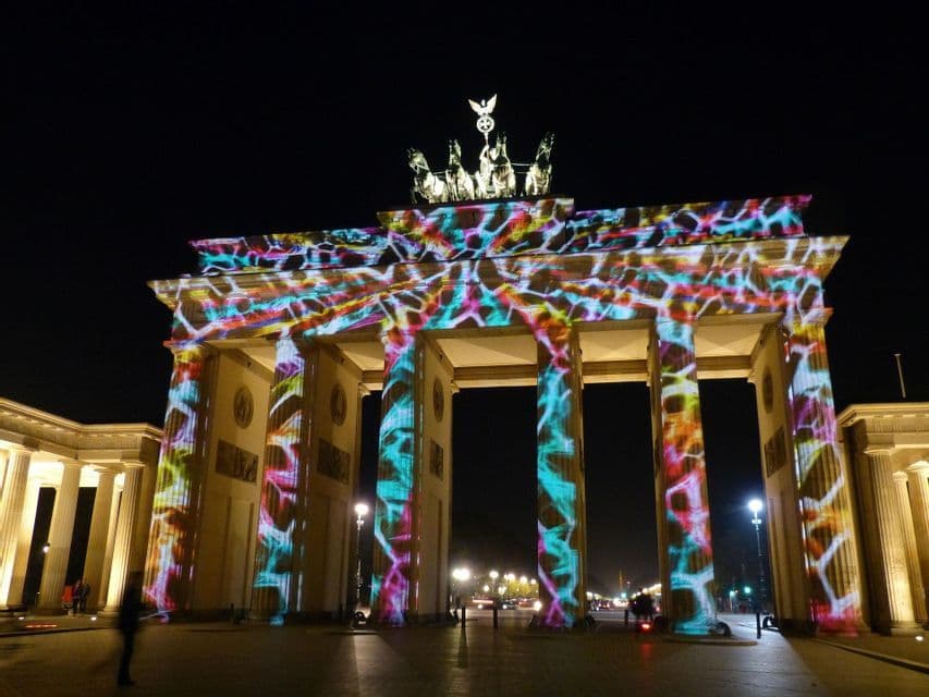 Un grande monumento neoclassico è illuminato di notte con una proiezione di luce astratta e colorata sulle sue colonne.
