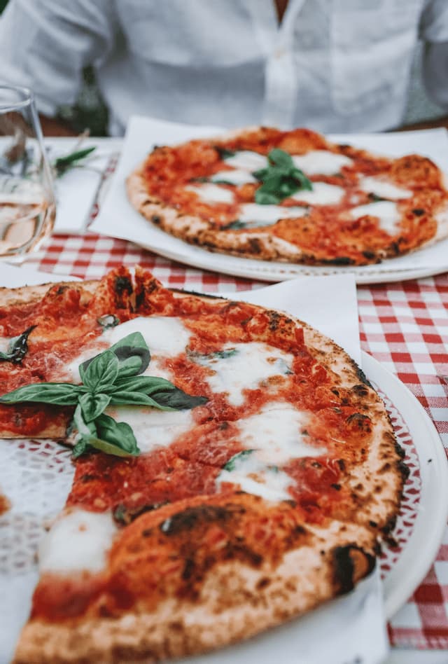 Primo piano di due pizze Margherita con basilico fresco, su una tovaglia a quadri rossi e bianchi in un ristorante.