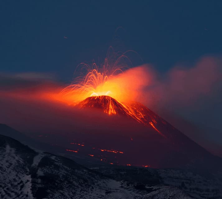 Un vulcano che erutta di notte, proiettando una pioggia di lava incandescente e scintille nel cielo scuro.