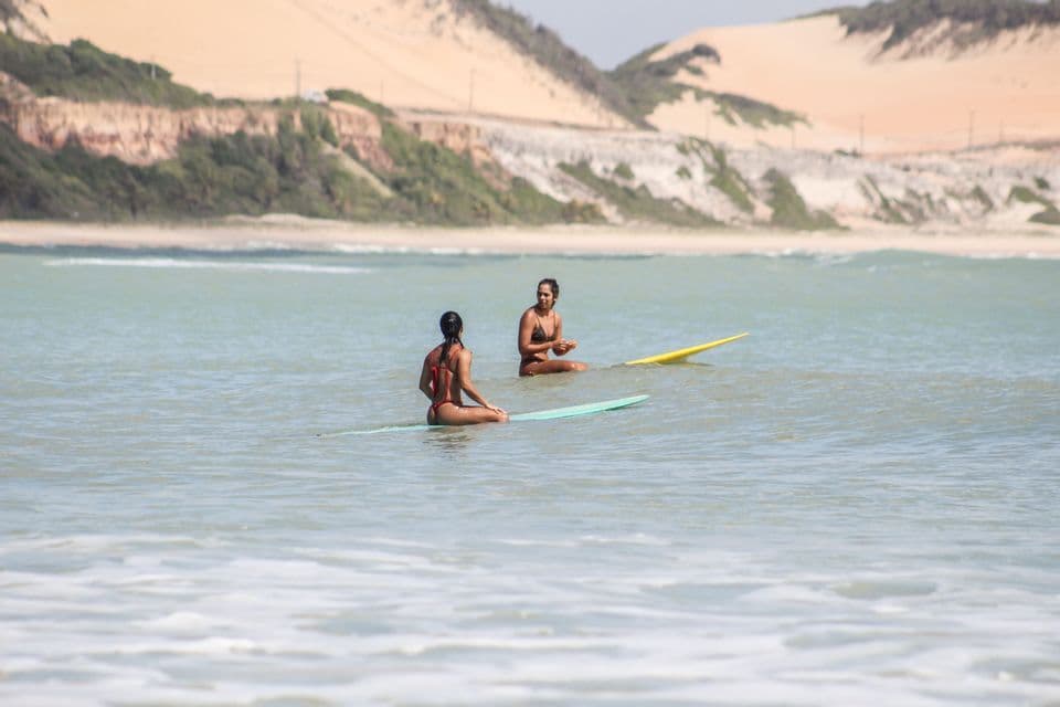 Due donne sono sedute sulle loro tavole da surf nell'oceano, prendendosi una pausa con scogliere sabbiose sullo sfondo.