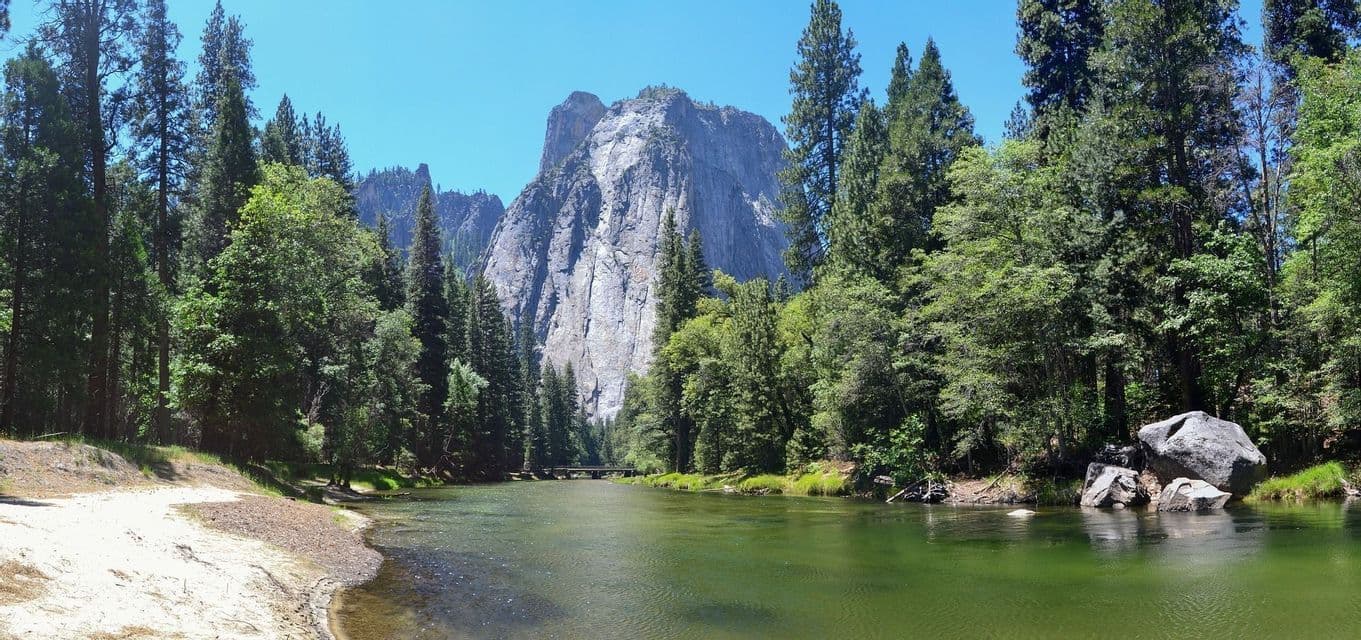 Un fiume tranquillo si snoda attraverso una pineta ai piedi di una imponente montagna di granito in una giornata di sole.