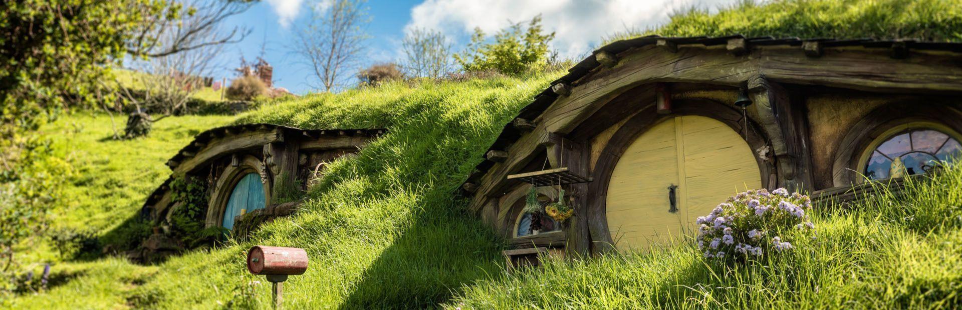 Two whimsical houses with round doors are built into a vibrant green hillside under a sunny sky.