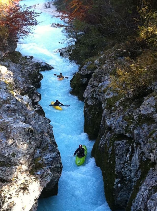 Eine WeRoad-Gruppe paddelt im Einerkajak einen schnell fließenden, leuchtend blauen Fluss hinunter, durch eine enge Felsenschlucht.