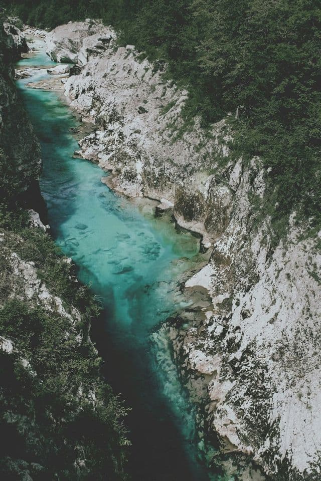 Blick von oben auf einen türkisfarbenen Fluss, der durch eine enge Schlucht fließt, mit hellen Felswänden und grüner Vegetation.