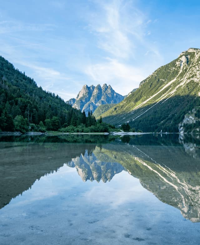 Una catena montuosa e la foresta circostante che si riflettono sulla superficie calma e limpida di un lago alpino.