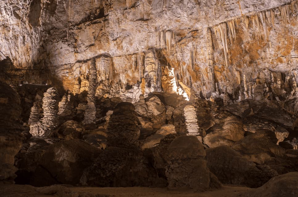 Una vasta grotta sotterranea piena di grandi stalattiti e stalagmiti illuminate.