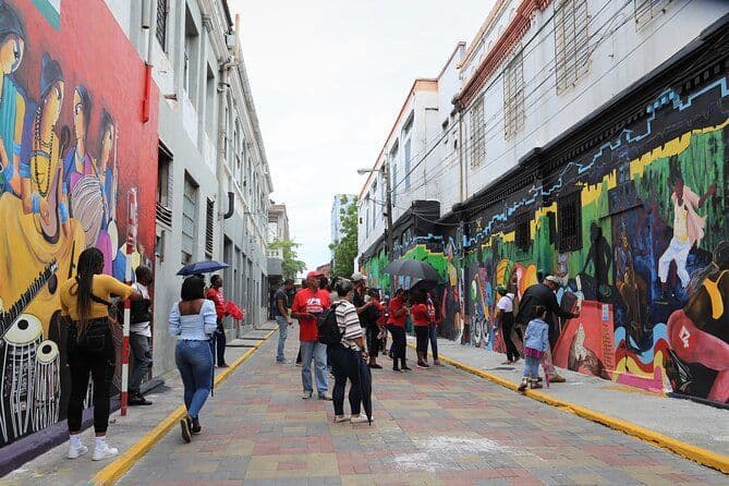Un viaje en grupo de WeRoad se encuentra en una calle pavimentada, admirando grandes murales coloridos pintados en las paredes de edificios adyacentes.