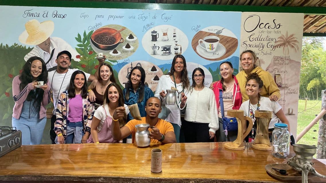 Un viaje en grupo de WeRoad sonríe para una foto durante una cata de café, posando detrás de un mostrador de madera con un mural al fondo.