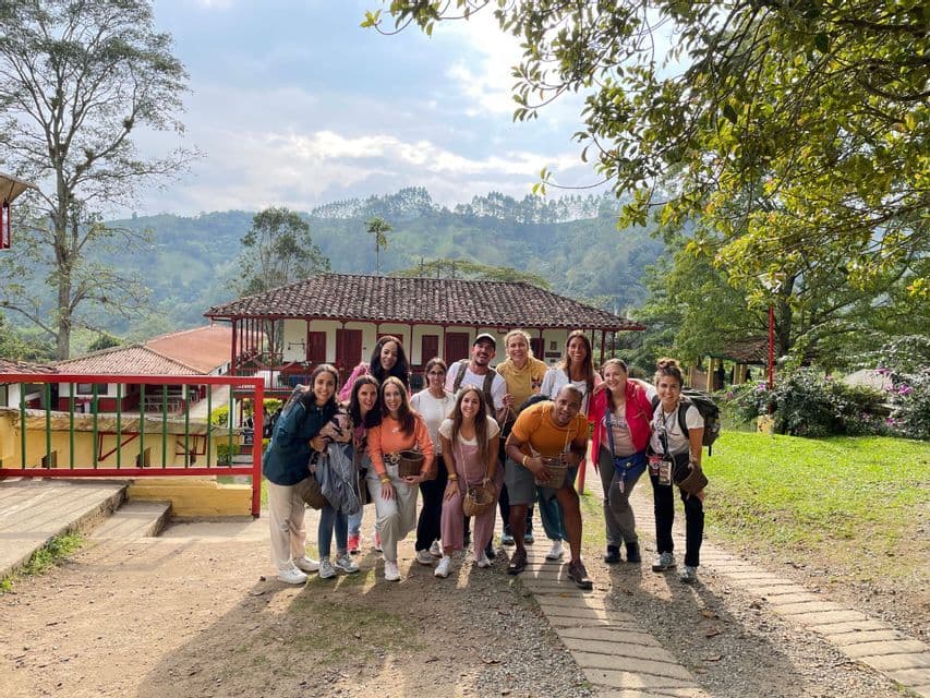 Un groupe WeRoad pose pour une photo sur un chemin devant un bâtiment rural, avec de luxuriantes collines vertes en arrière-plan.
