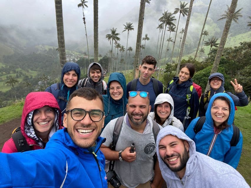 A WeRoad group trip takes a selfie on a foggy day, with a green valley and tall palm trees behind them.