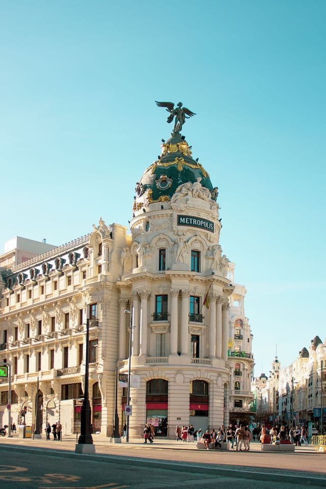 Vue en contre-plongée du majestueux bâtiment Metropolis, avec sa statue ailée et son dôme obscur, se découpant sur un ciel bleu pur.