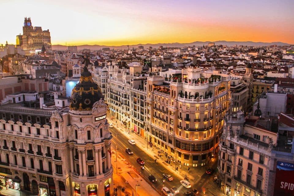 Vue plongeante sur une ville européenne dense, avec des bâtiments ornés et des rues animées par la circulation au coucher du soleil.