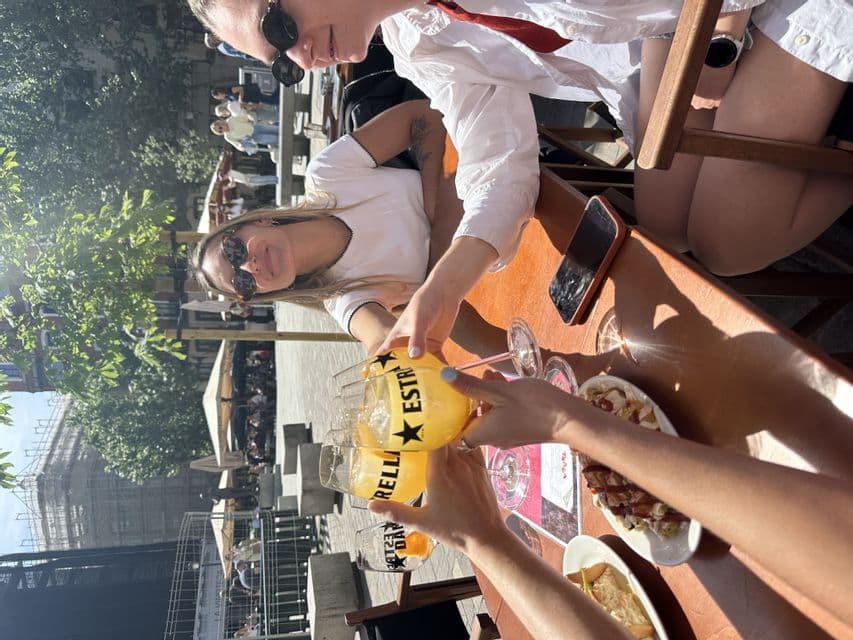 Un voyage de groupe WeRoad trinquant avec de grands verres d'une boisson jaune à la table ensoleillée d'un café en plein air.