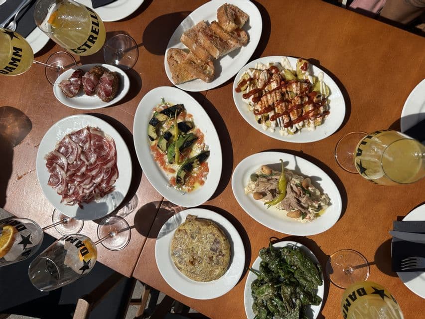 Vue plongeante sur une table couverte d'assiettes de tapas espagnoles, dont de la tortilla et du jambon cru, et des verres de boissons.