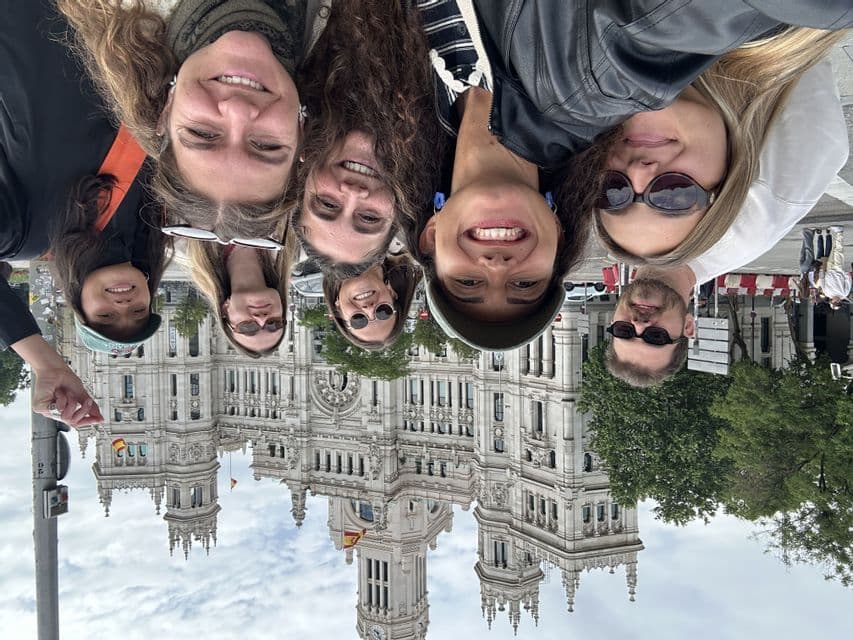 Un selfie à l'envers d'un groupe WeRoad en voyage, souriant devant un bâtiment historique orné.