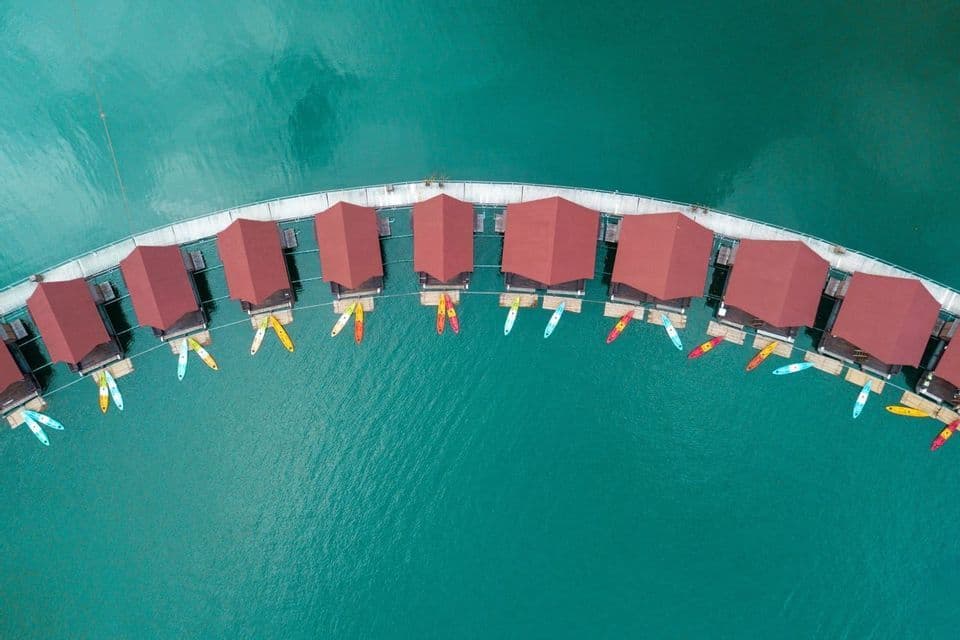 Une vue aérienne de bungalows flottants incurvés aux toits rouges et de kayaks amarrés sur une eau turquoise.