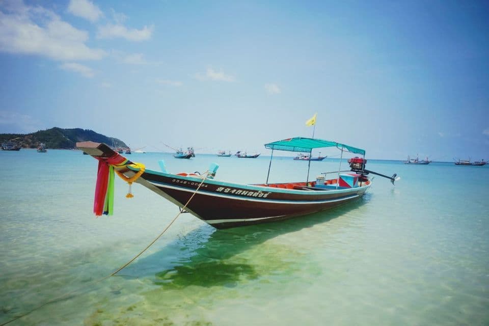 Une pirogue traditionnelle, ornée de rubans, flotte sur une eau turquoise calme, avec une île verdoyante à l'horizon.