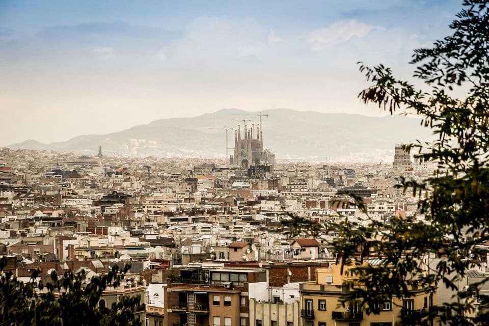Una veduta aerea di una vasta città con una grande cattedrale in costruzione e montagne sullo sfondo.