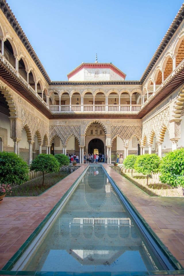 Un viaggio di gruppo WeRoad in un cortile di palazzo sontuoso, con una lunga piscina riflettente e dettagliati archi moreschi.