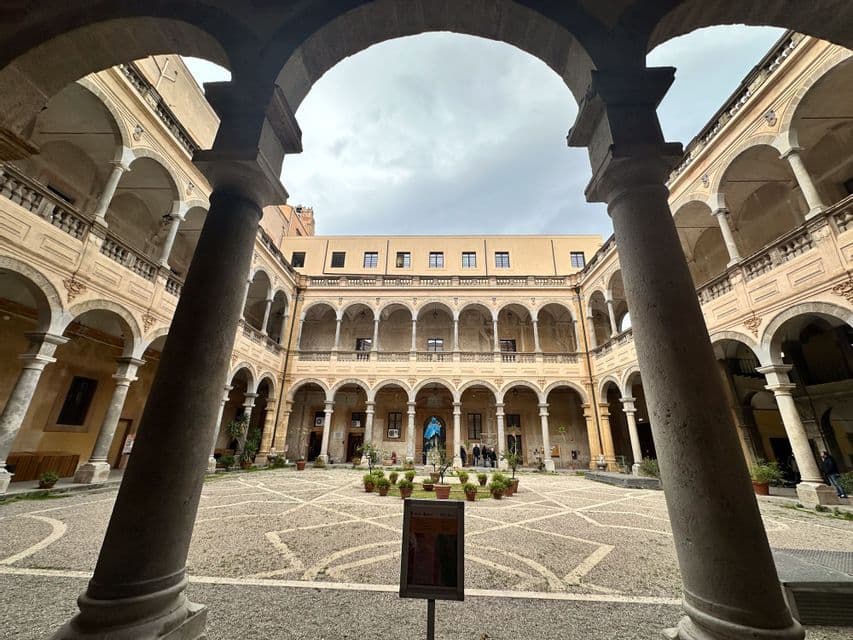 Cortile di un edificio storico con colonnati ad arco, inquadrato tra due grandi colonne in primo piano sotto un arco.
