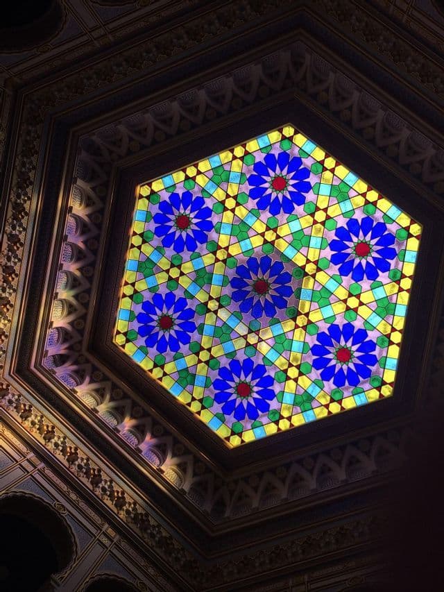 Una vista desde abajo de una cúpula de techo de vitral hexagonal con un colorido diseño floral geométrico.