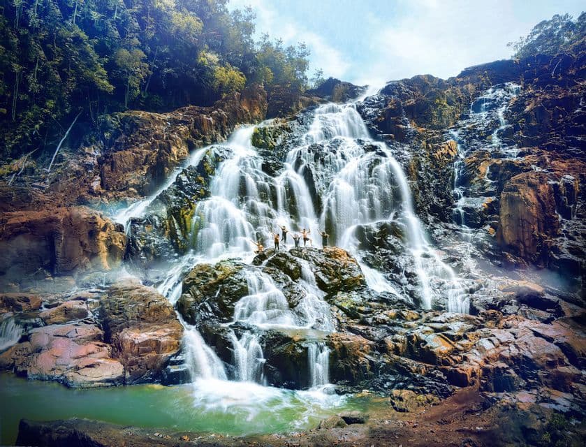 Un gruppo WeRoad in posa sulle rocce di fronte a una grande cascata a più livelli che scende da una montagna.