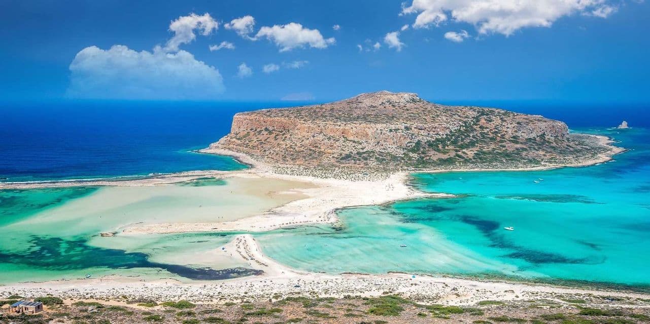 Una vista panoramica di un'isola rocciosa collegata a una lingua di sabbia bianca, che crea una laguna turchese accanto al mare blu profondo.