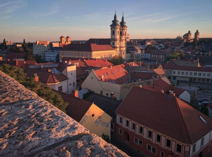 Una vecchia città europea con tetti rossi e chiese è bagnata dalla luce dell'ora d'oro, vista dall'alto.