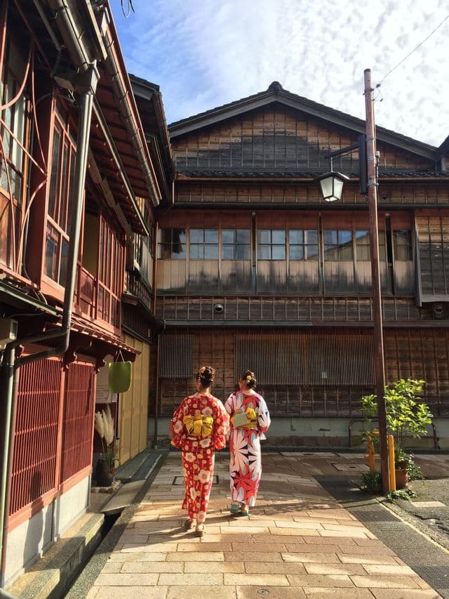 Due donne in kimono floreali colorati camminano lungo una strada stretta tra tradizionali edifici giapponesi in legno.