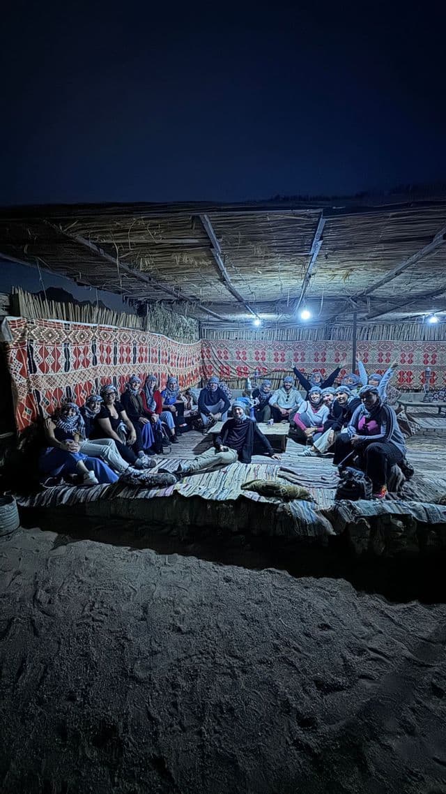 A WeRoad group trip sits together on a raised platform inside a rustic shelter with patterned textile walls at night.