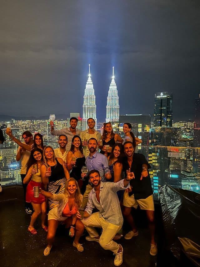 Un gruppo WeRoad posa per una foto su un tetto di notte, con torri gemelle illuminate sullo sfondo.