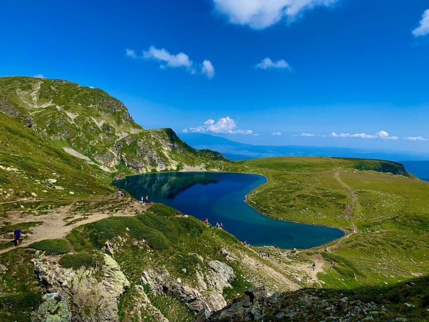 Un voyage de groupe WeRoad en randonnée sur les sentiers entourant un lac de montagne d'un bleu profond par une journée ensoleillée.