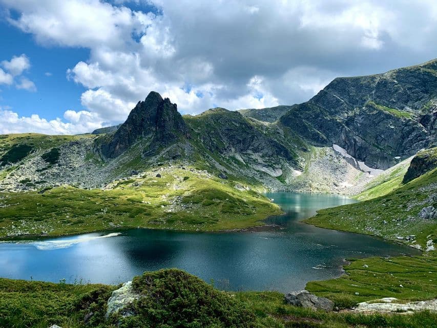 Deux lacs alpins reliés sont nichés dans une vallée entre des montagnes vertes et rocheuses, sous un ciel bleu nuageux.