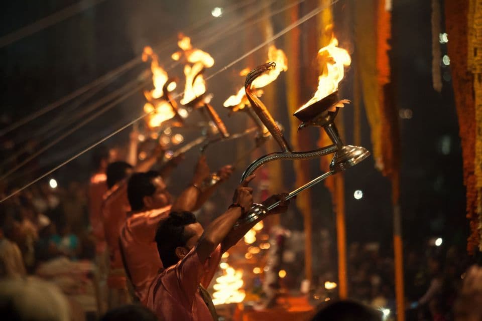 Hombres con túnicas naranjas sostienen grandes lámparas con forma de cobra en llamas durante una ceremonia nocturna ante una multitud.