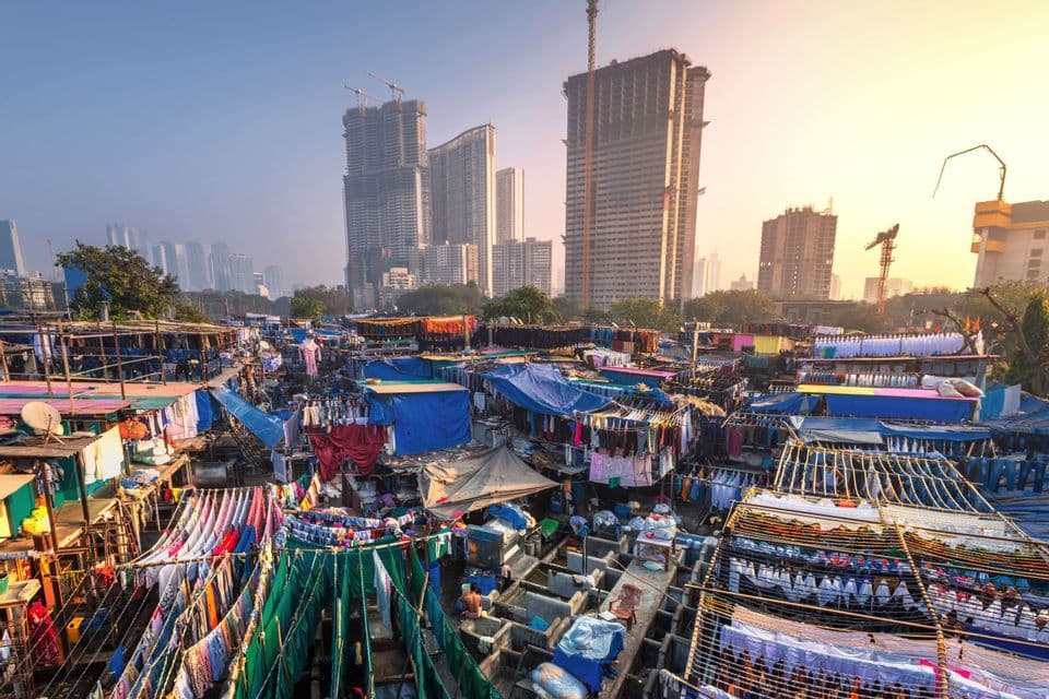 Vista aérea de una lavandería al aire libre con ropa secándose en tendederos, con un telón de fondo de rascacielos modernos de la ciudad al amanecer.