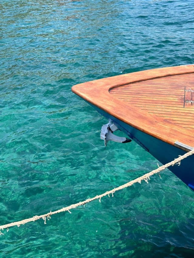 Der Bug eines Holzbootes mit sichtbarem Anker schwimmt auf klarem, türkisfarbenem Wasser.
