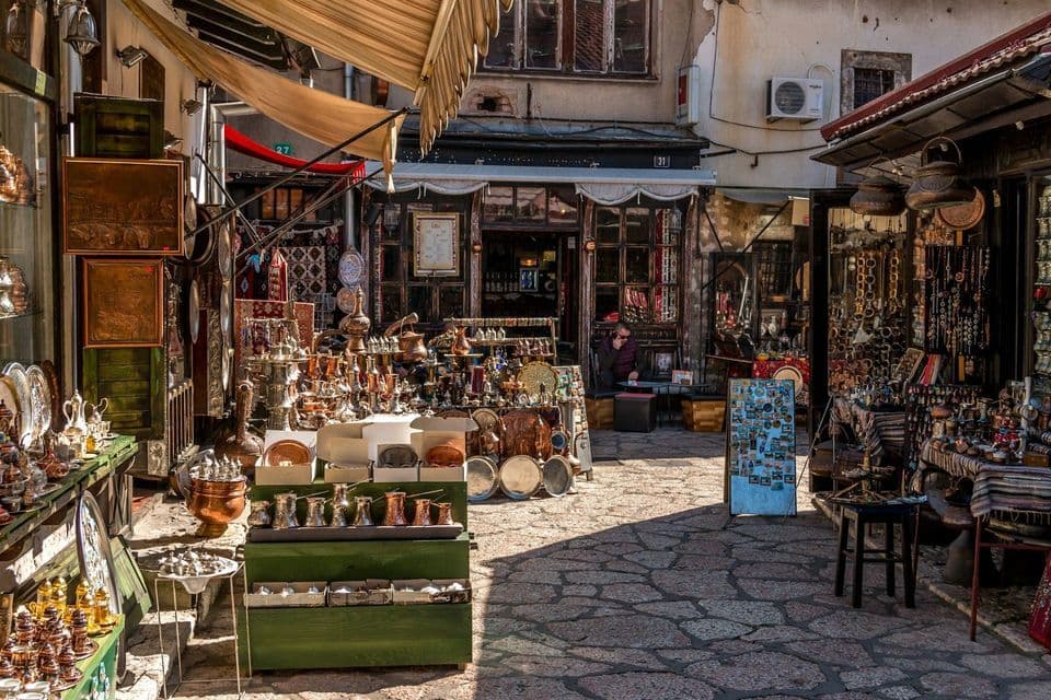 Marktstände bieten traditionelle Kupferwaren und Schmuck zum Verkauf an, entlang einer sonnigen Kopfsteinpflastergasse.