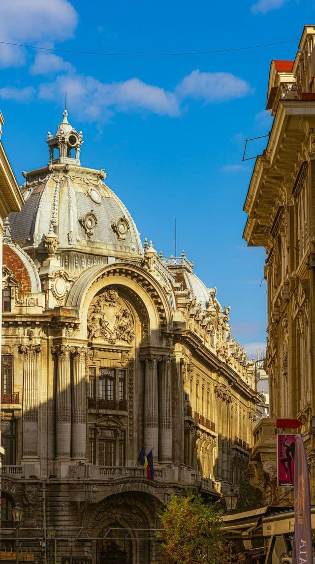 Ein reich verziertes historisches Gebäude mit großer Kuppel und Säulen, von einer schmalen Gasse unter strahlend blauem Himmel gesehen.