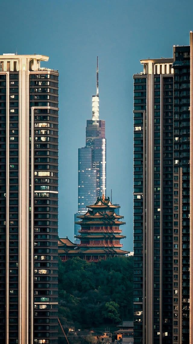 Una pagoda tradizionale su una collina verde e un moderno grattacielo sono incorniciati da due grattacieli residenziali sotto un cielo azzurro e limpido.