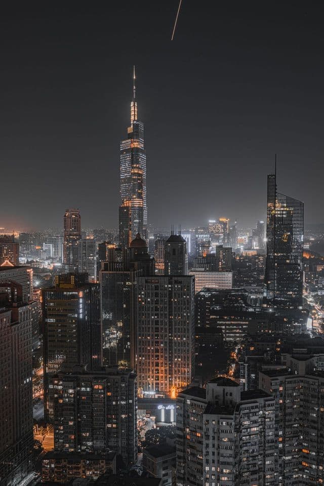 Un paesaggio urbano tentacolare di grattacieli illuminati di notte, con una torre prominente che si staglia nel cielo scuro.