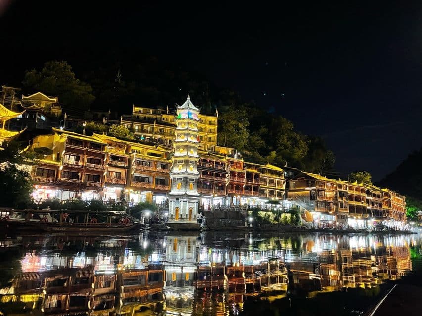 Una città lungo il fiume con una pagoda centrale, tutta illuminata di notte, con le sue luci che si riflettono nell'acqua calma.