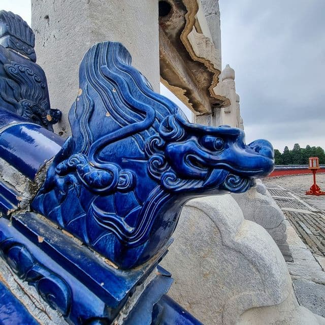 Primo piano di una scultura di testa di drago in ceramica blu vibrante su una struttura di pietra consumata.