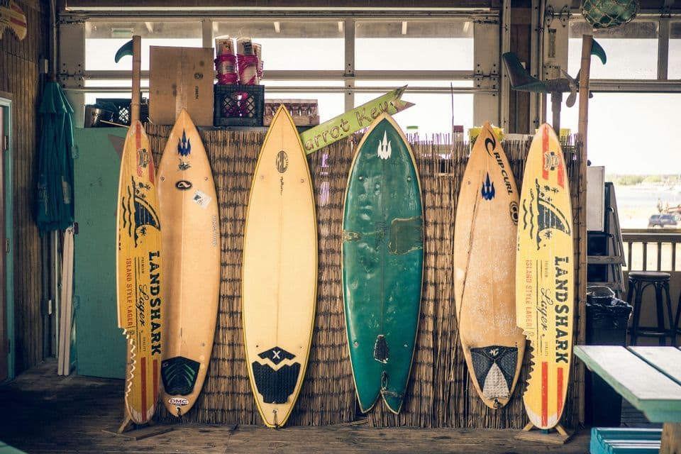 Seis tablas de surf coloridas de varios diseños alineadas contra una pared de paja dentro de una cabaña de playa.